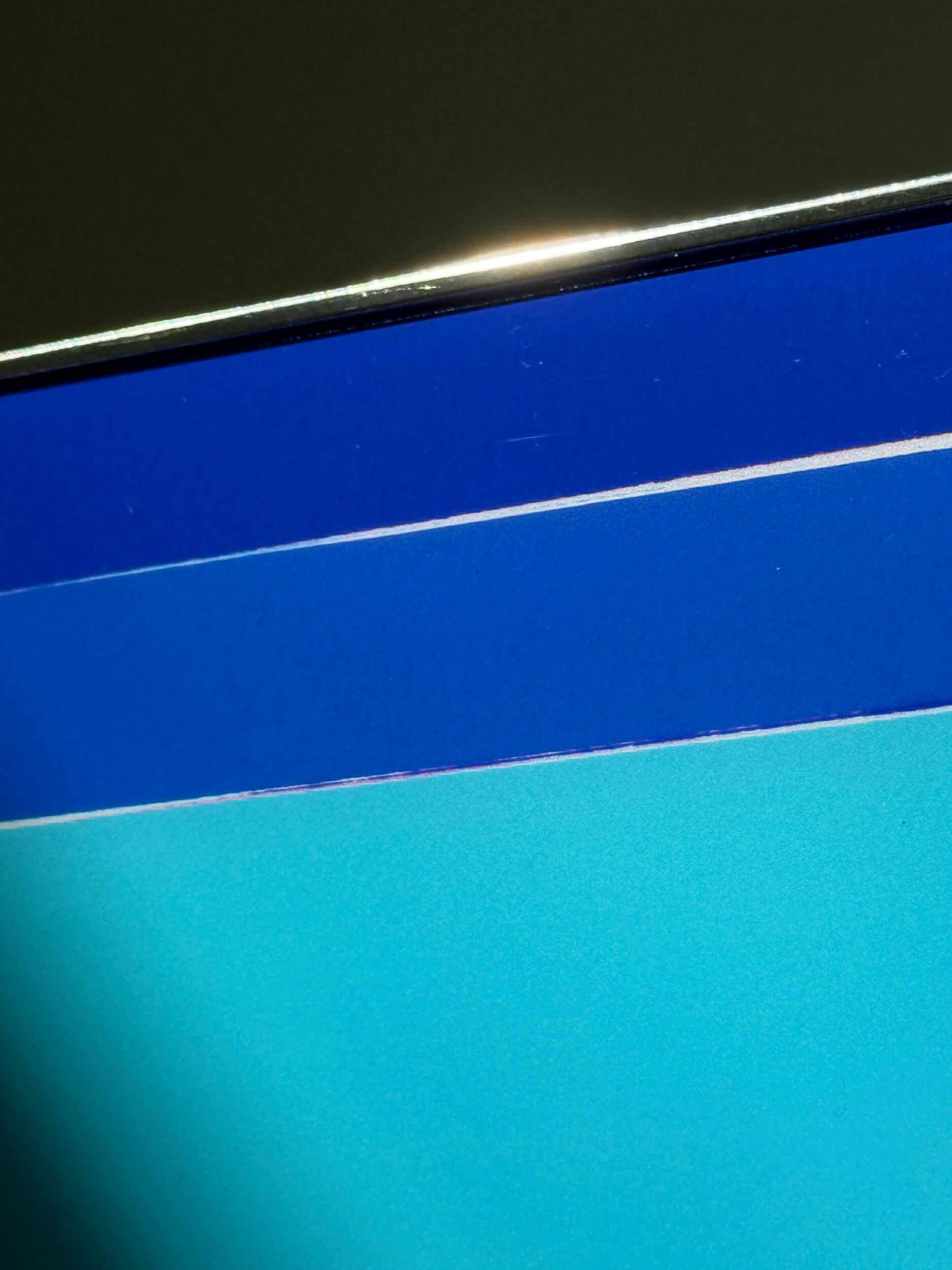 A close-up of the top corner of a flat screen displaying shades of blue and turquoise, with a metallic edge visible at the top.