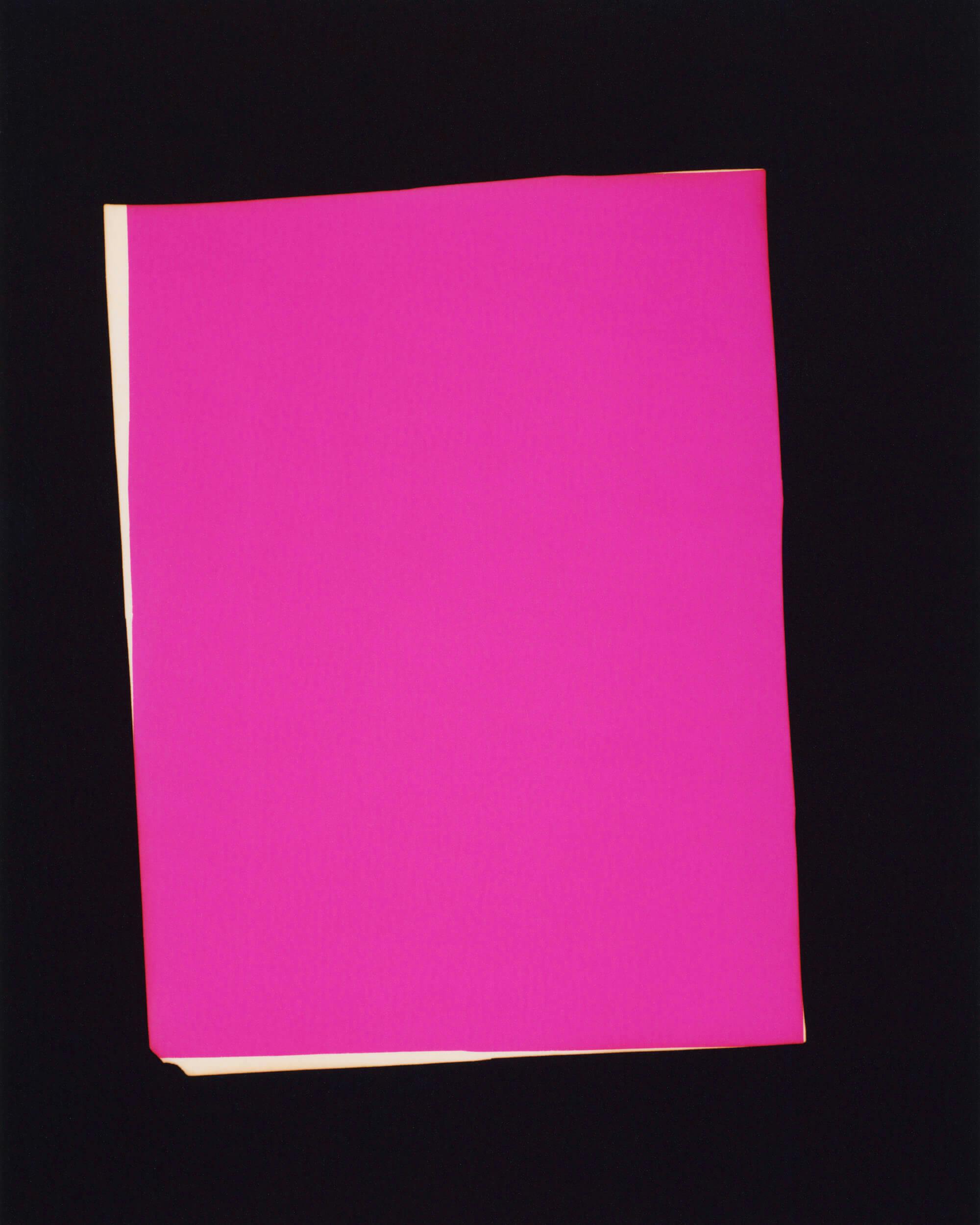 A single sheet of bright pink paper is positioned against a black background, with a small portion of a beige sheet visible at the edge underneath.