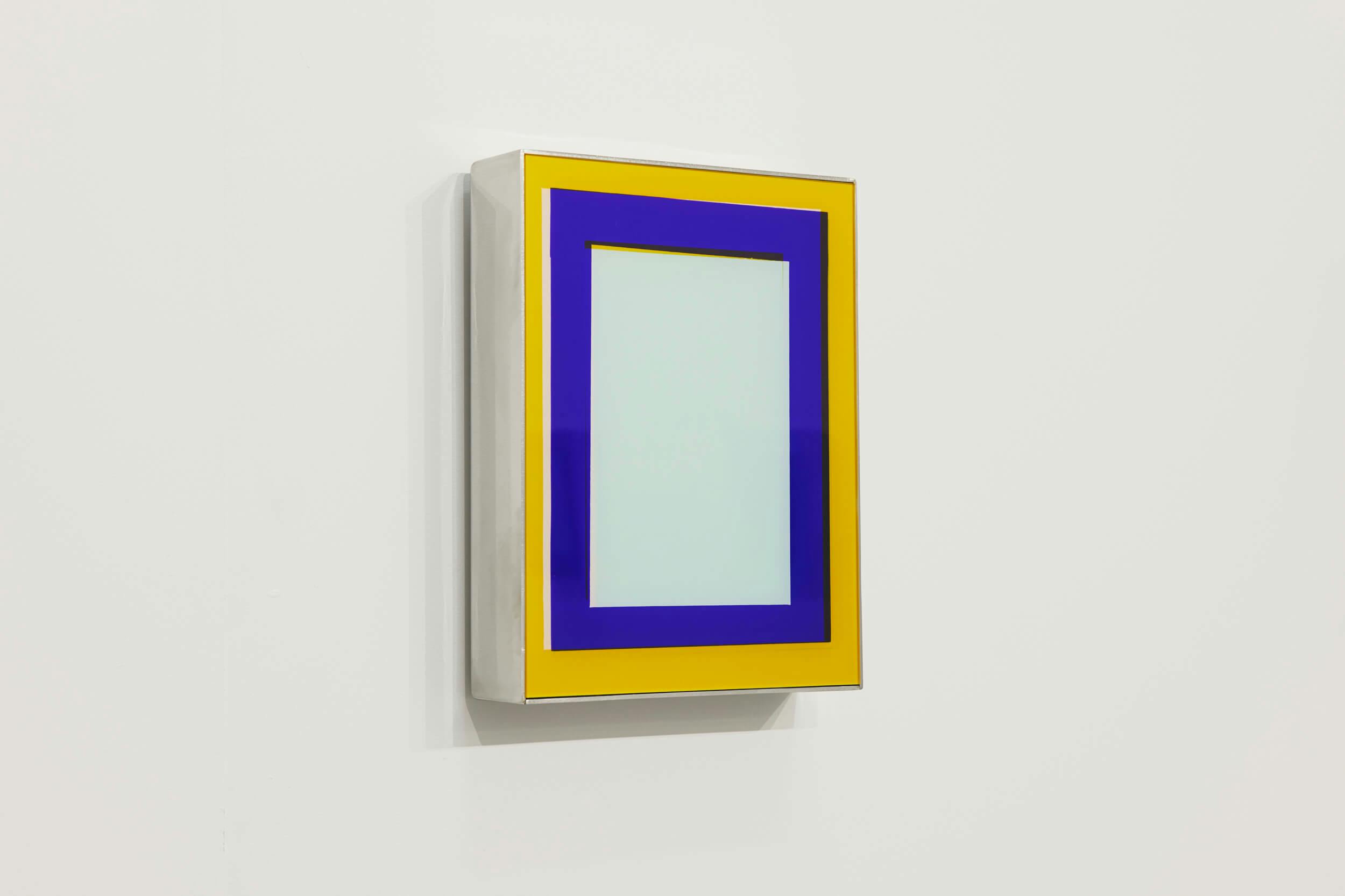 A rectangular artwork mounted on a white wall features a light blue center bordered by a thick blue band and a yellow outer frame, all enclosed in a deep, box-like frame.