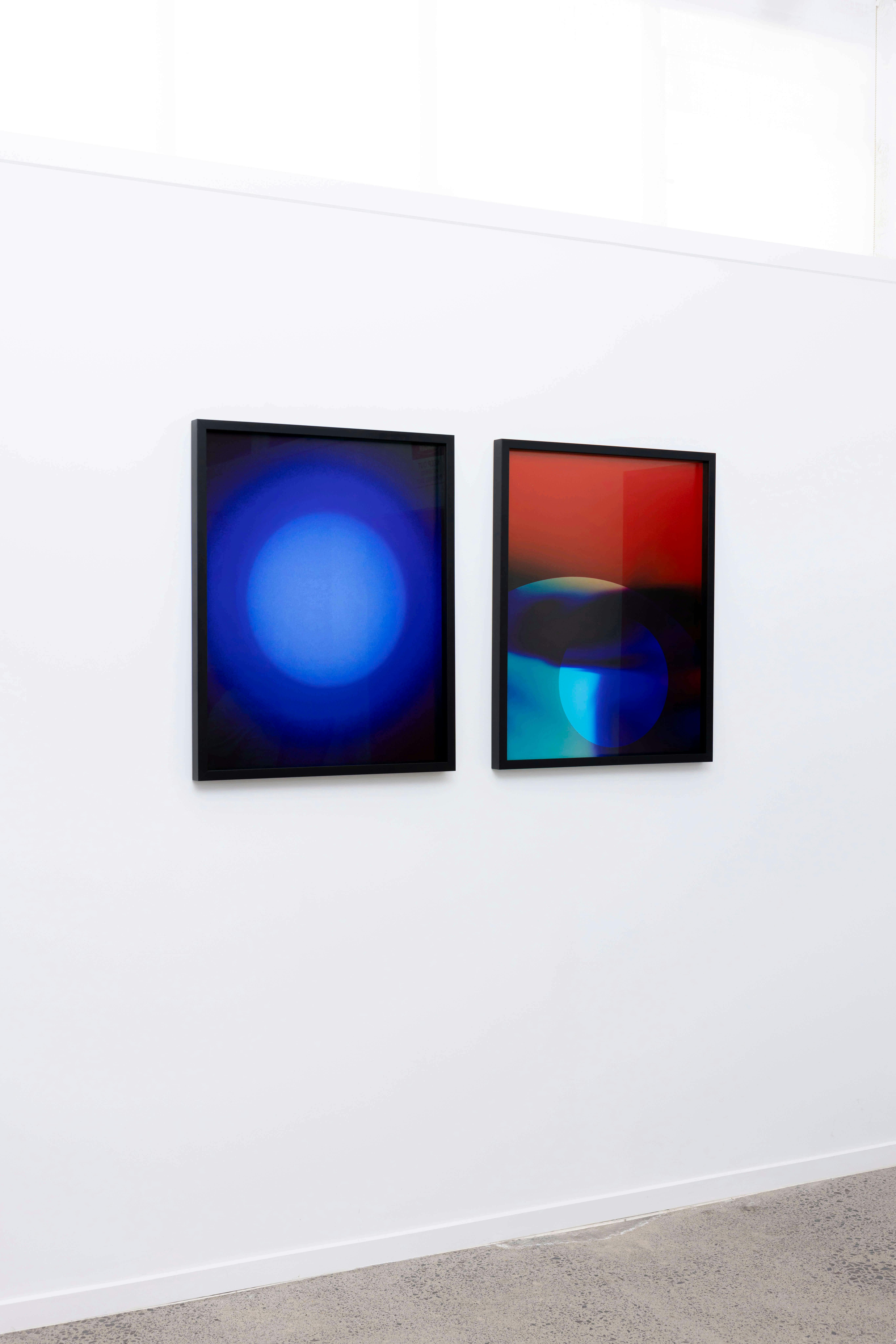 Two framed abstract artworks hang side by side on a white wall. The left image features a large blue circle, while the right image displays overlapping circular shapes in blue, red, black, and purple tones.