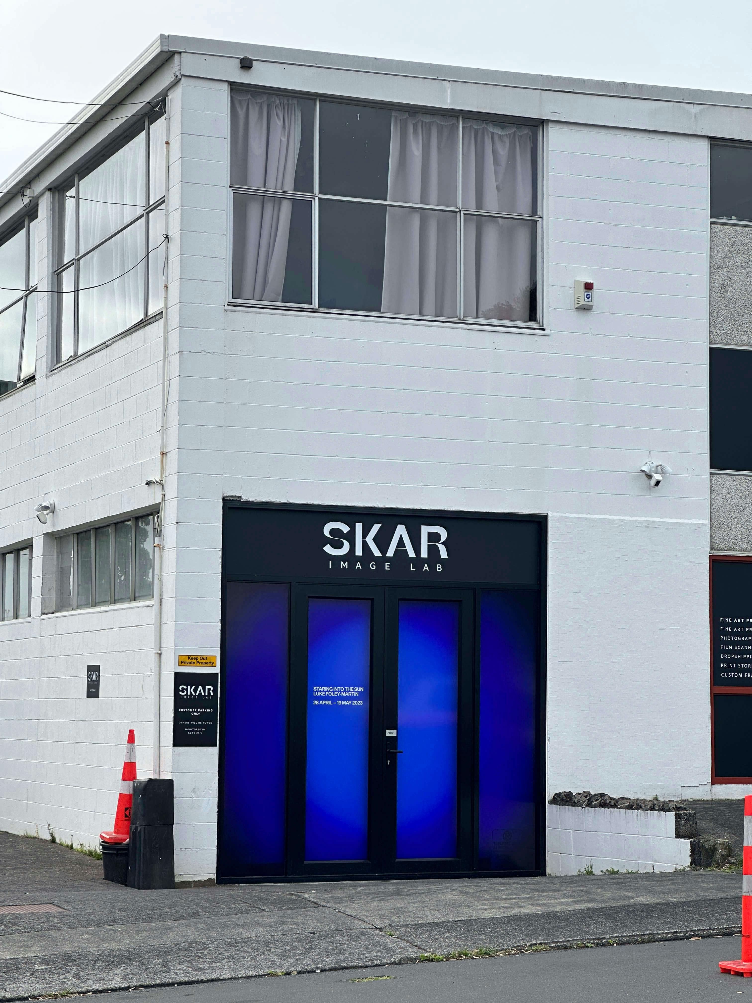 A white two-story building with large windows and a black entrance labeled