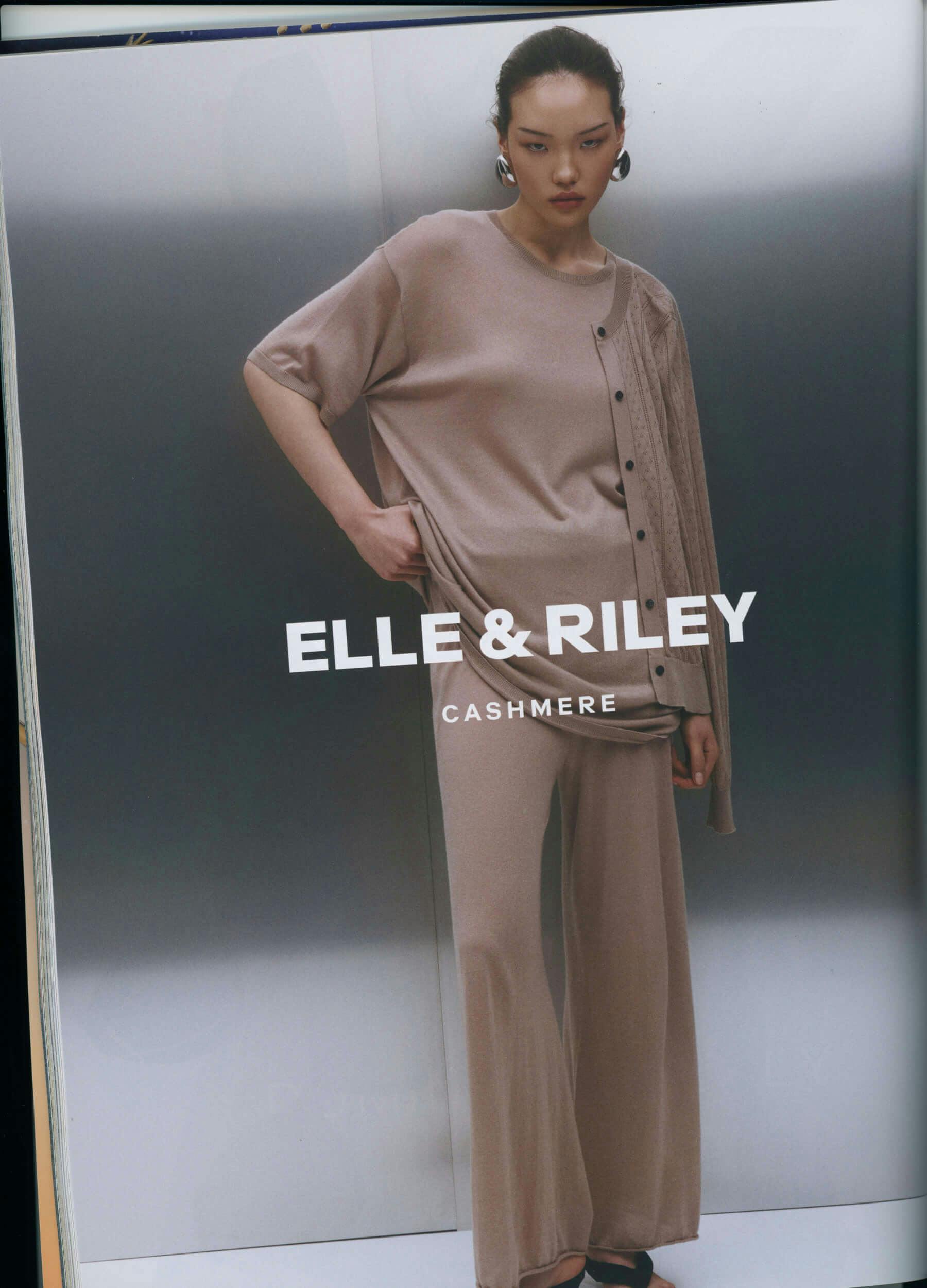 A person stands against a neutral gradient background wearing a loose-fitting beige cashmere top and matching wide-leg pants. One sleeve of a matching cardigan is draped over their shoulder. Text reads 