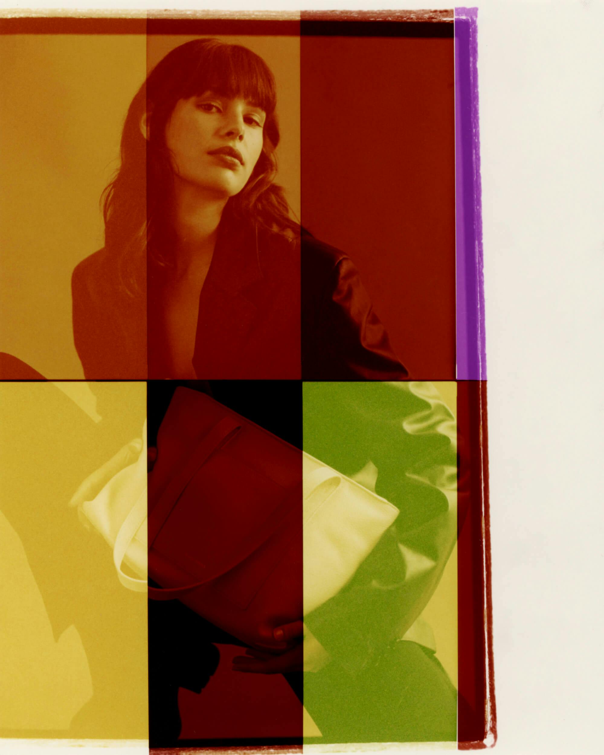 A woman with dark hair and bangs looks at the camera, wearing a dark blazer. She holds a white handbag. The image is overlaid with red, yellow, green, and purple translucent rectangles.