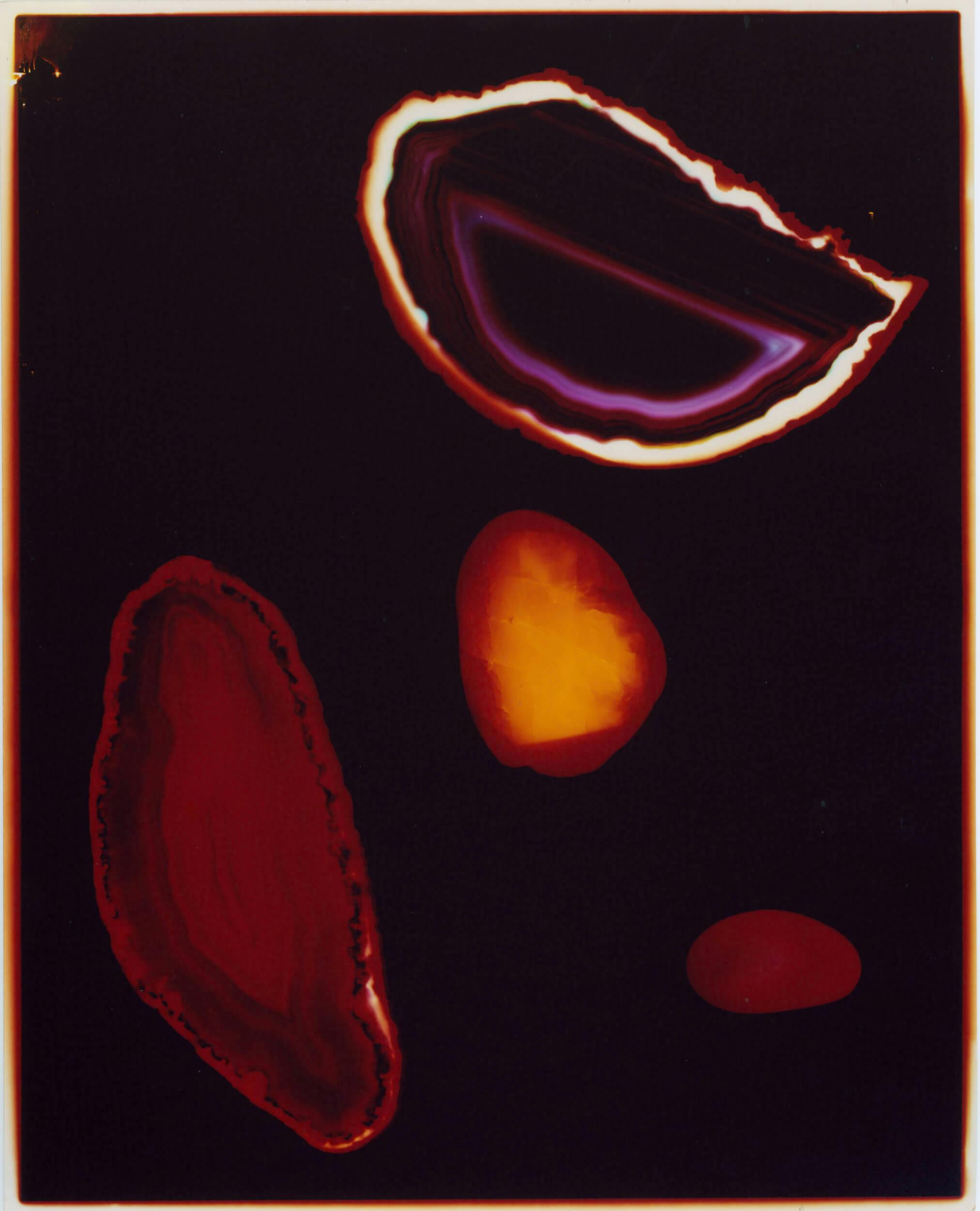 A dark background with four brightly colored, irregular shapes resembling minerals or geodes in red, purple, yellow, and orange tones, each displaying layered or glowing edges.