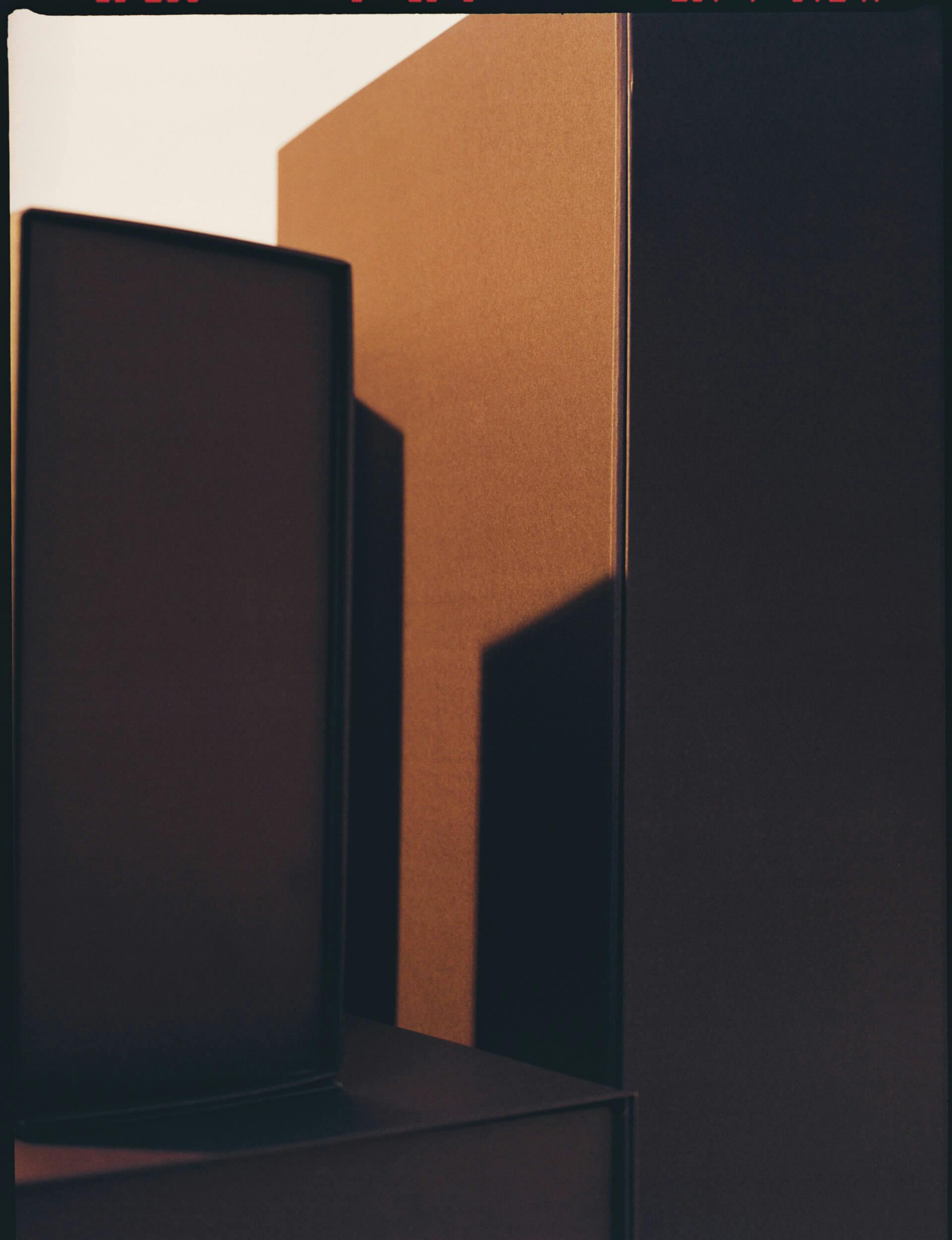 Rectangular and square objects in shades of brown are arranged close together, with light casting sharp shadows on their surfaces. The composition creates an abstract, geometric appearance.