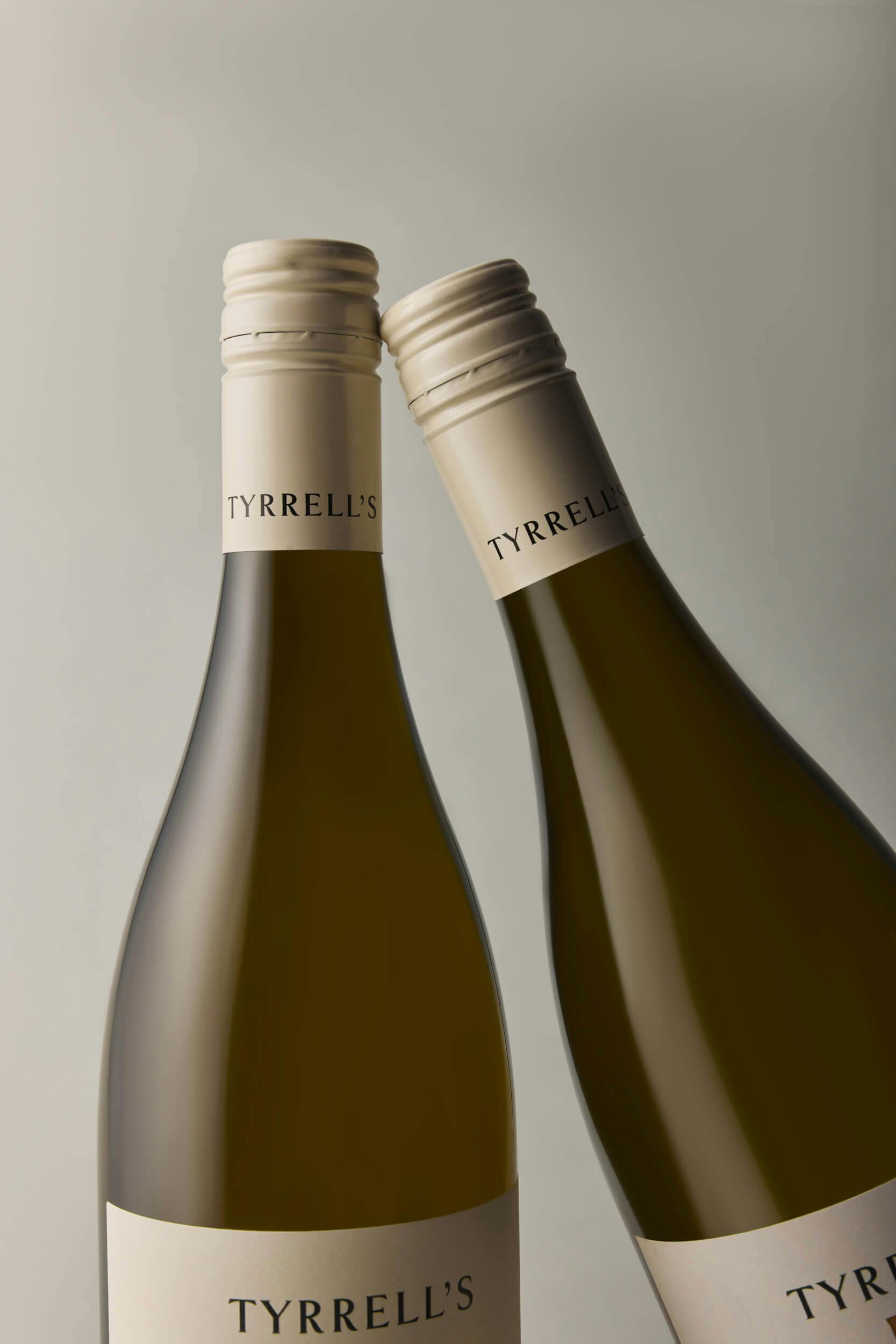 Two bottles of Tyrrell’s wine with beige screw caps are positioned close together against a plain, light grey background. The labels and caps are clearly visible.
