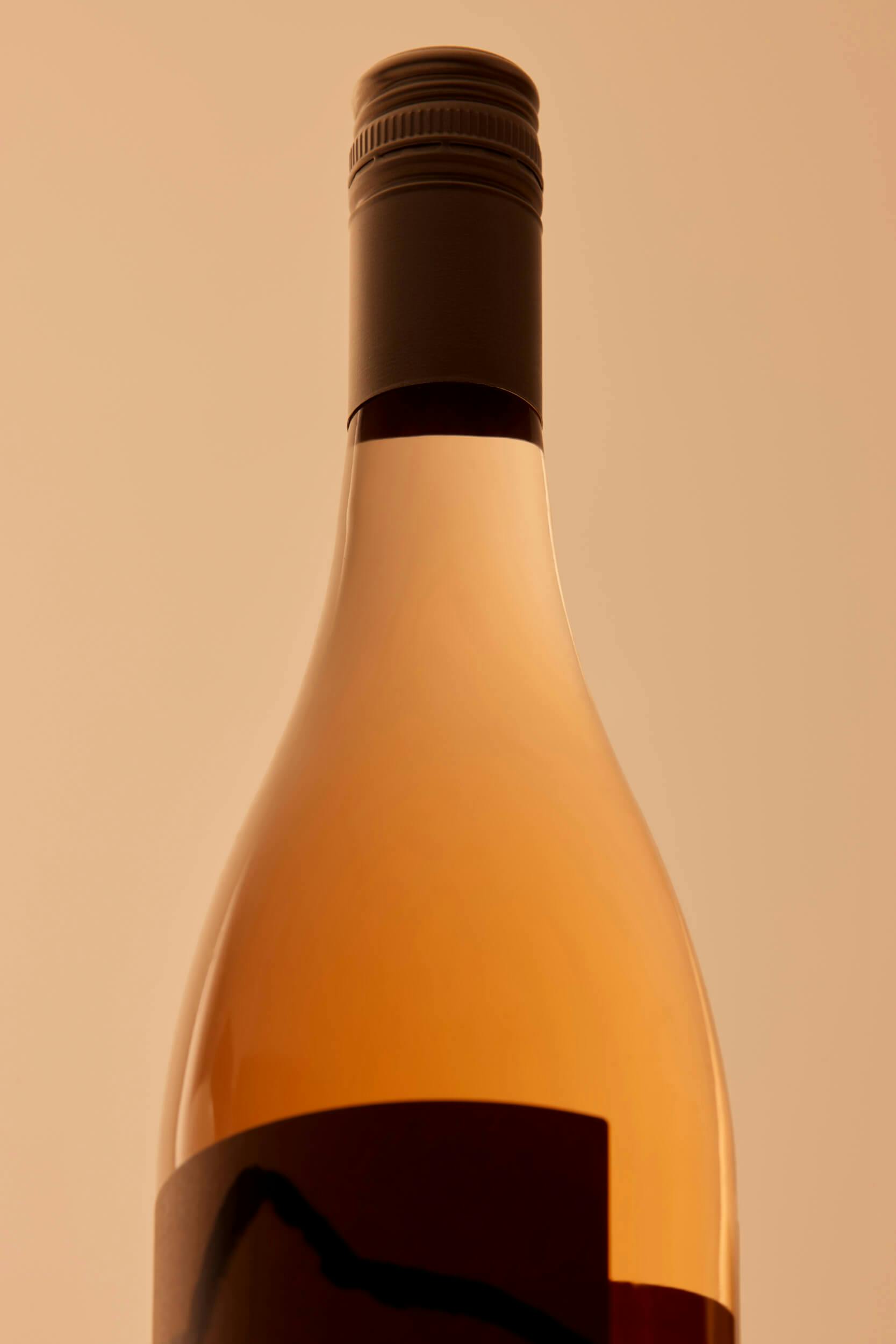 A close-up of a sealed wine bottle with a dark screw cap, set against a plain beige background. The bottle appears to contain a rosé or light-colored wine.